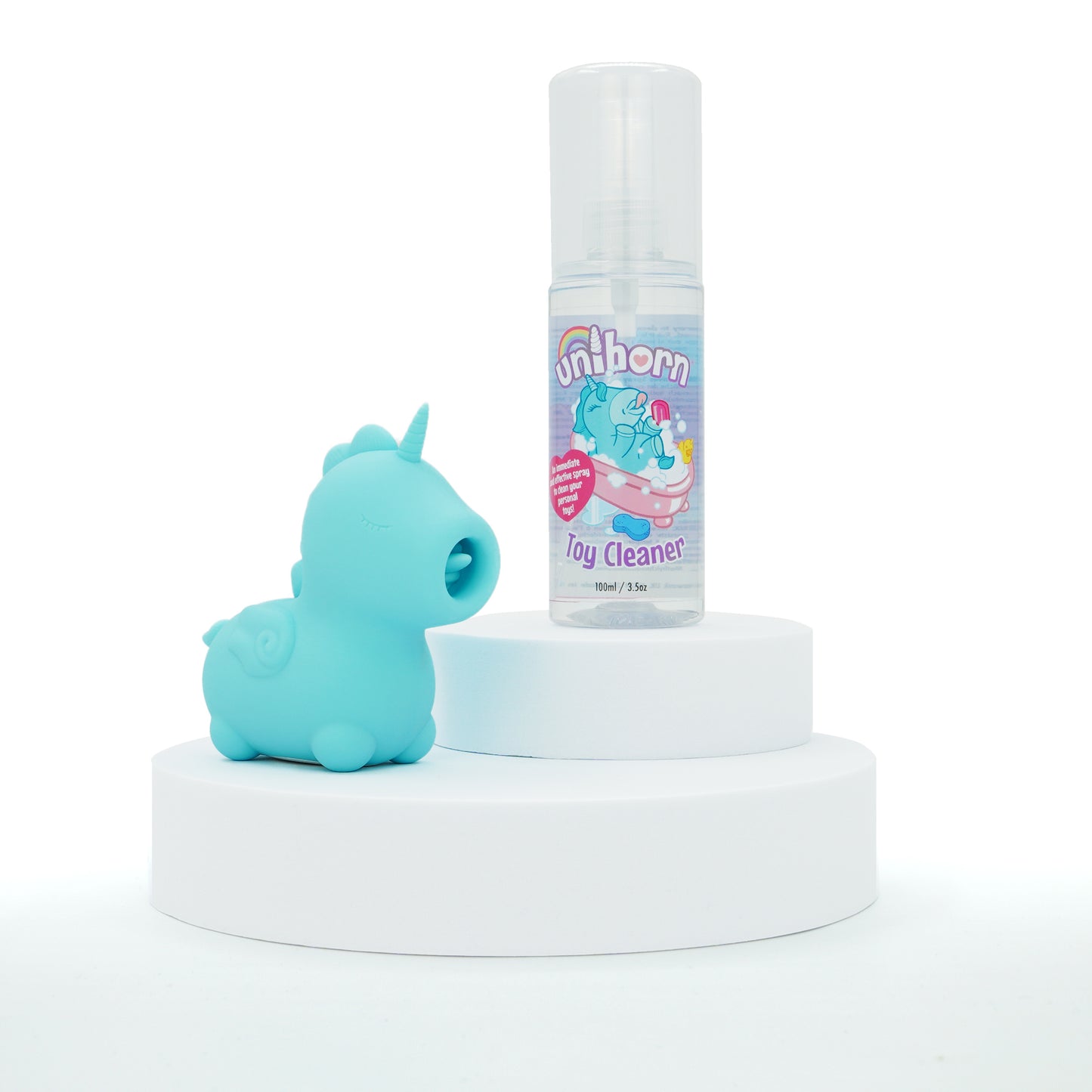 A 2-tiered white podium on a white background. On the bottom sits Mount N' Peak and slightly above the Unihorn Toy Cleaner bottle.