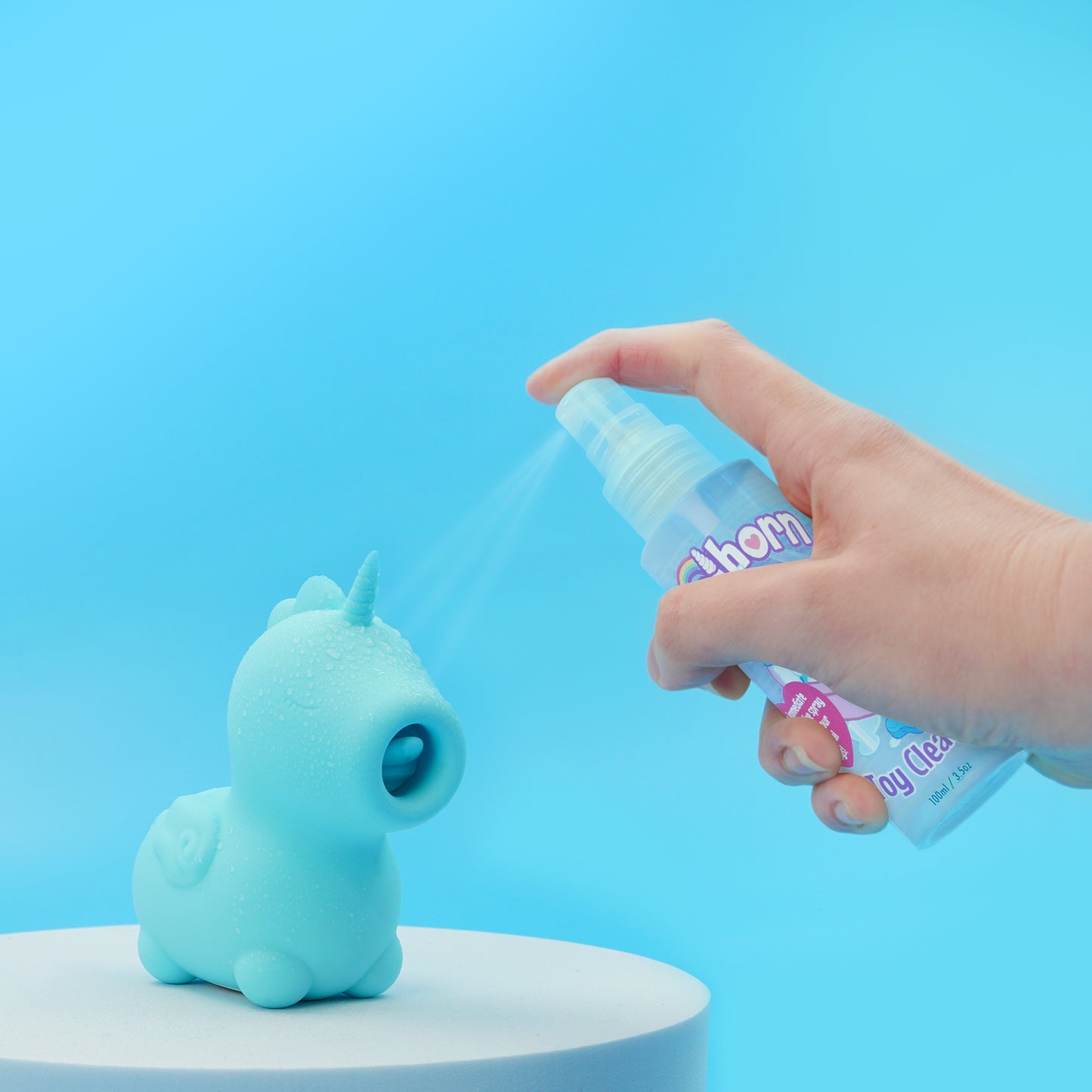Unihorn Toy Cleaner being sprayed on a Mount N' Peak Unihorn which is stood on a white pedestal on a blue background