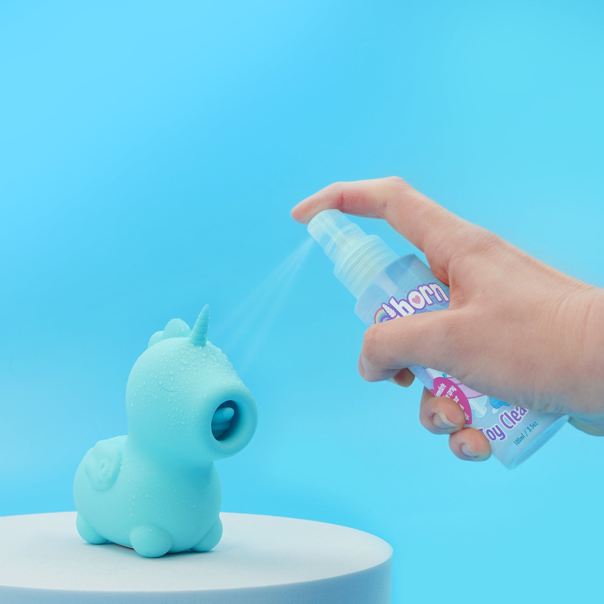 Unihorn Toy Cleaner being sprayed on a Mount N' Peak Unihorn which is stood on a white pedestal on a blue background