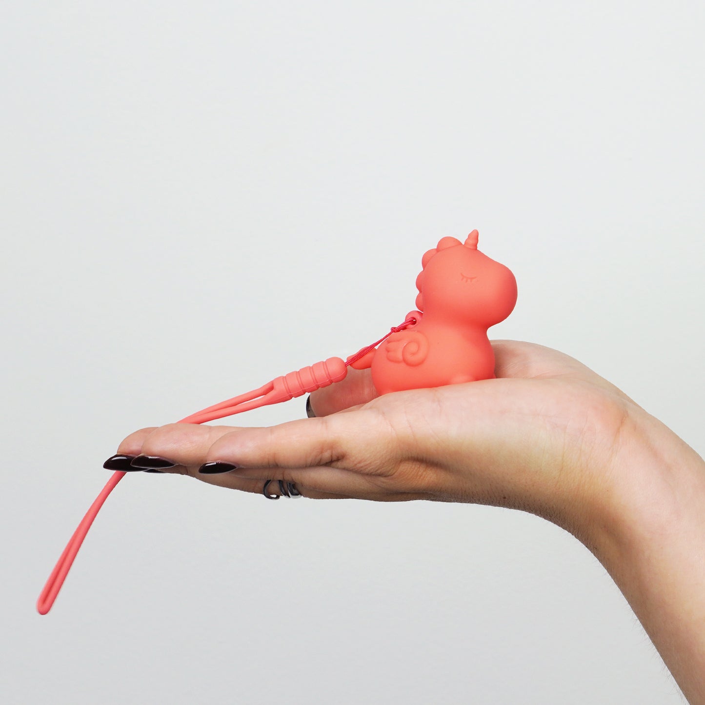 Peachy Pony sat on the palm of a hand with the keychain hanging over on a white background