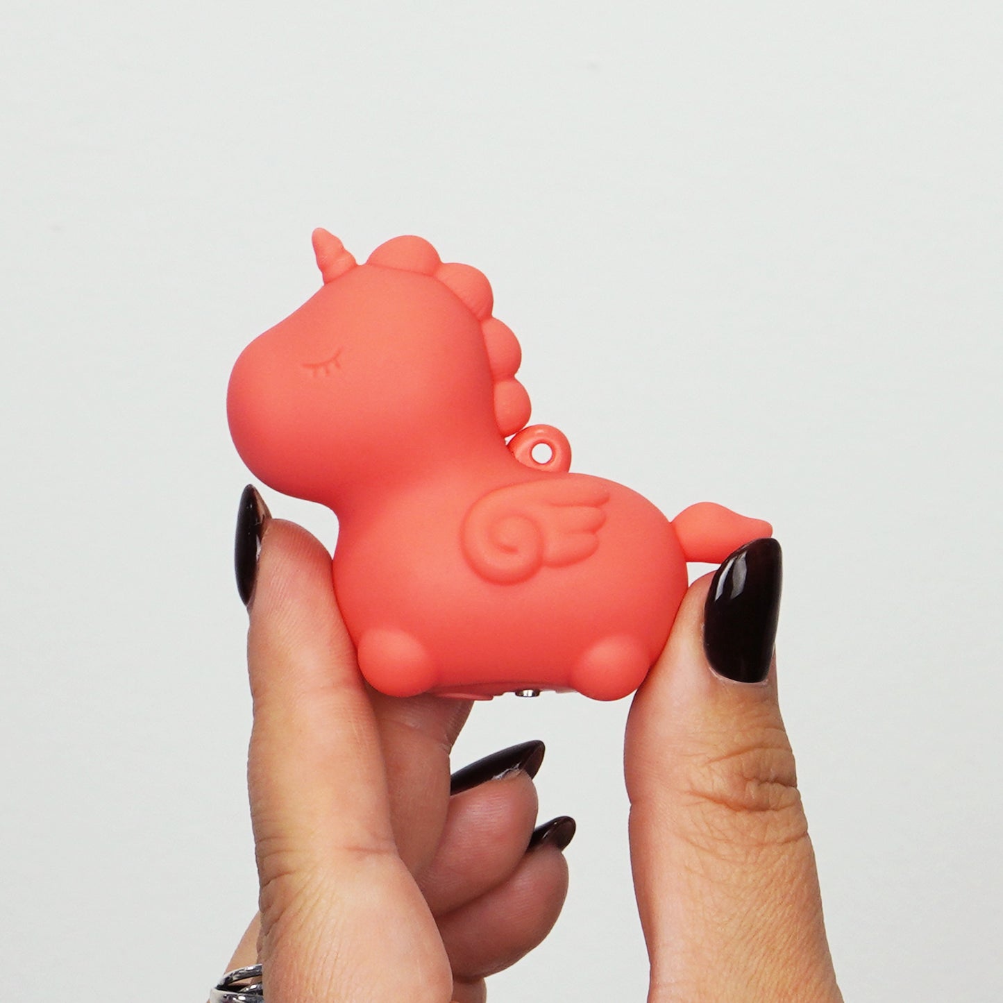 Peachy Pony Unihorn being held by the thumb and pointer finger on a white background