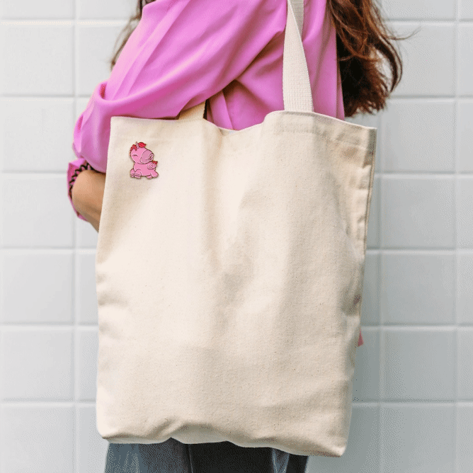 Gif zooming in and out on the pink Heart Throb Unihorn pin badge which is pinned to a canvas tote bag on the shoulder of a girl in a pink top