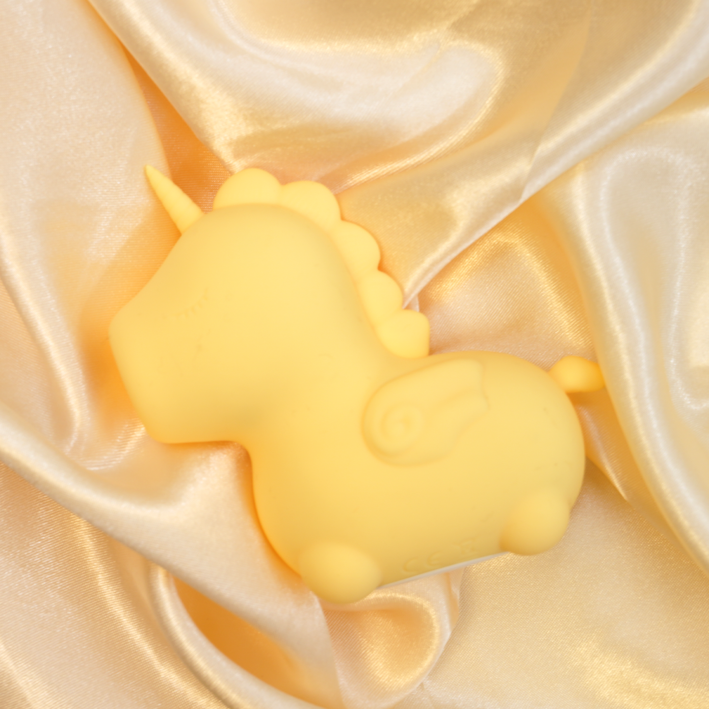 Yellow Bean Blossom clitoral vibrator laid facing the left, on a yellow satin sheet