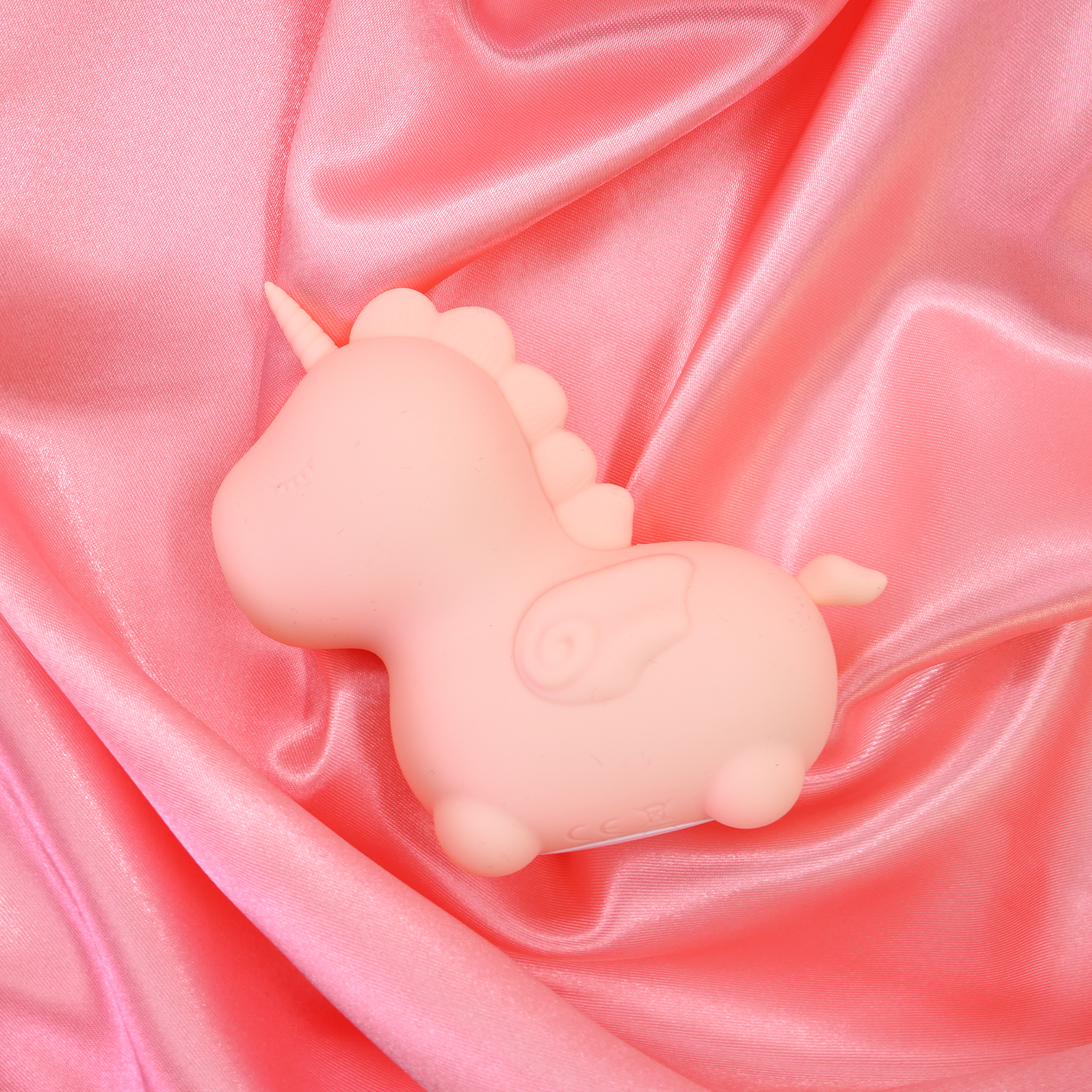 Heart Throb Unihorn vibrator, laid down facing the left on a pink satin sheet