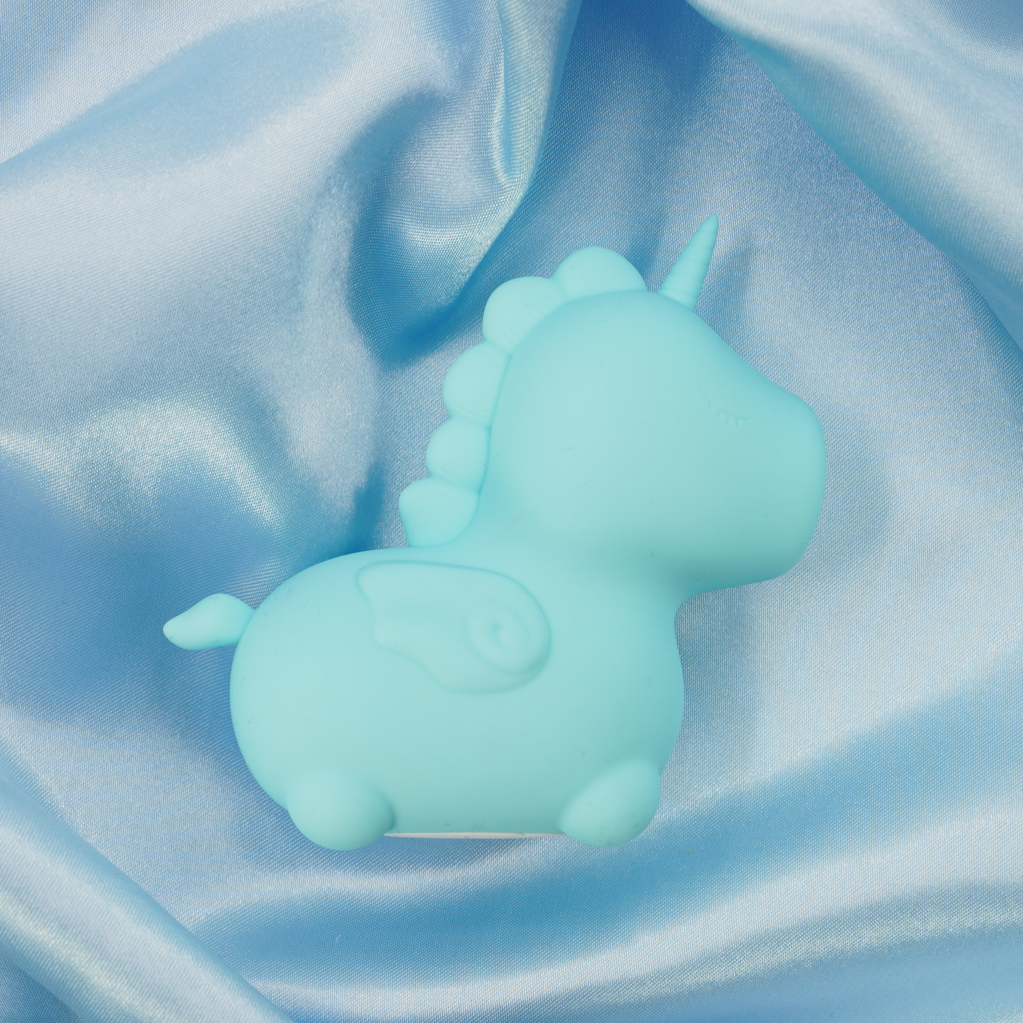 Blue Mount N' Peak Unihorn vibrator facing the right, laid on a blue satin sheet