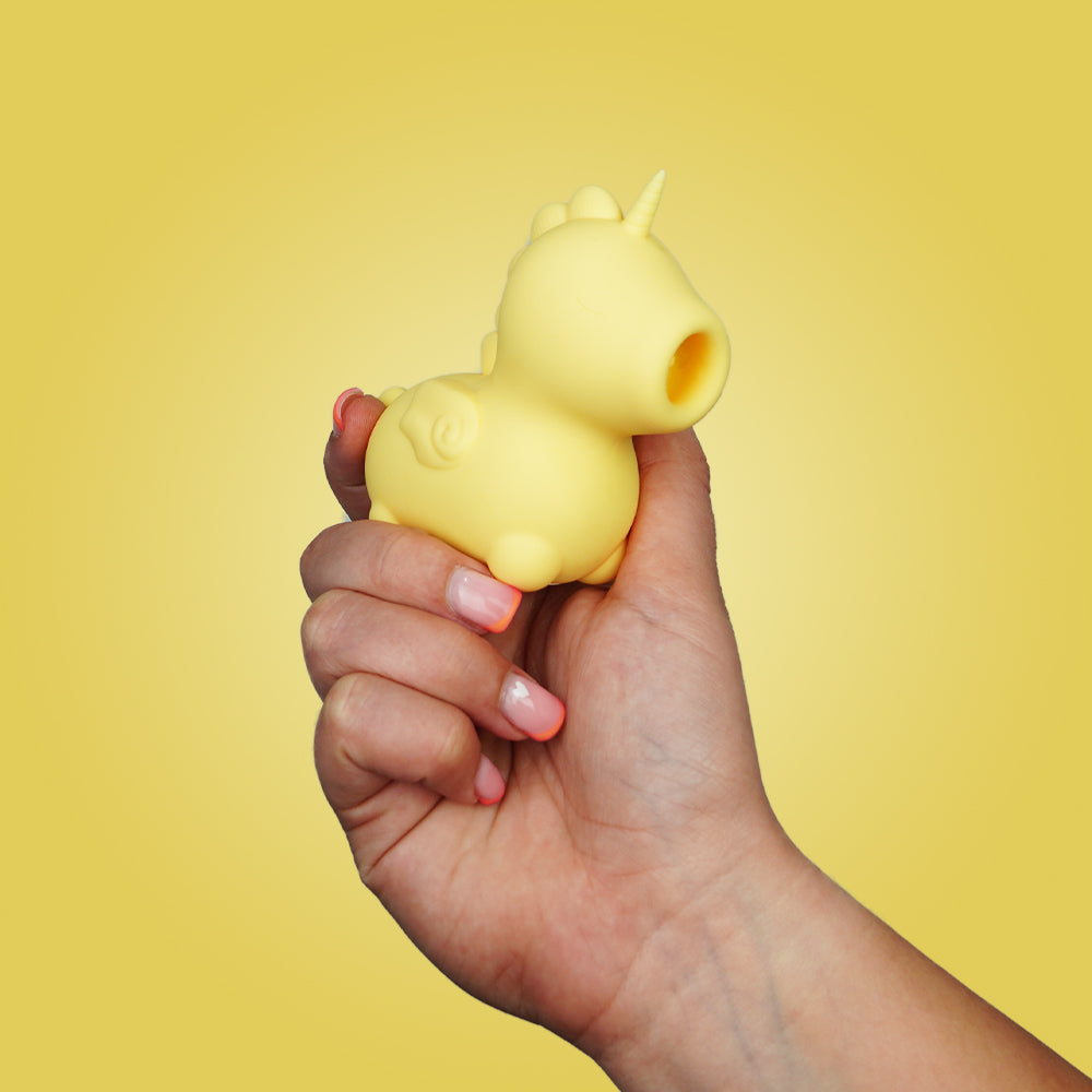 Hand holding a yellow Bean Blossom Unihorn, facing slightly to the right, on a bright yellow background