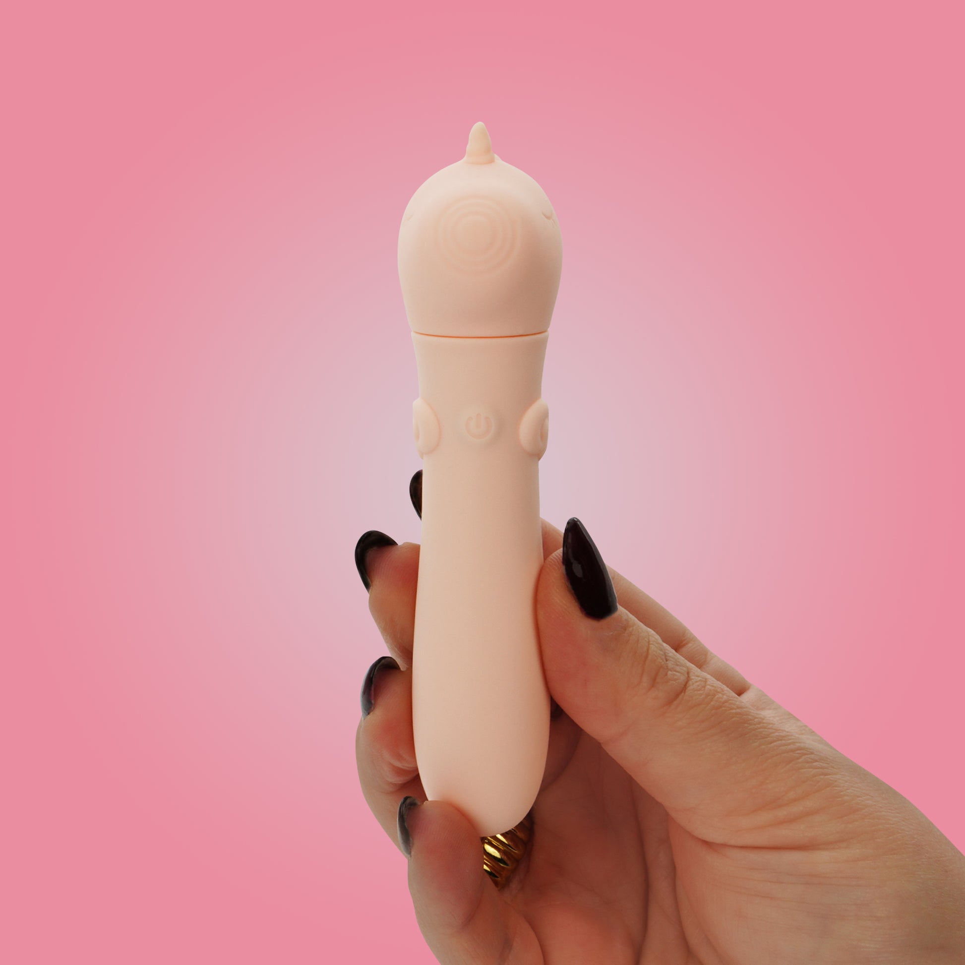 Hand with black nails, holding Heart Throb bullet vibrator on a bright pink background