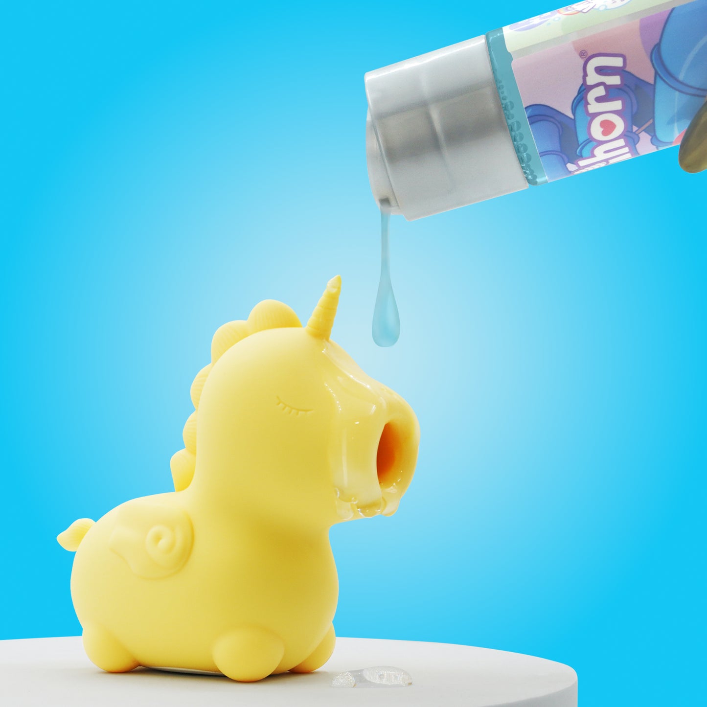 Close up of Bean Blossom stood on a white table in the bottom left-hand corner with lube being poured onto the mouthpiece from the top right-hand corner and a bright blue background