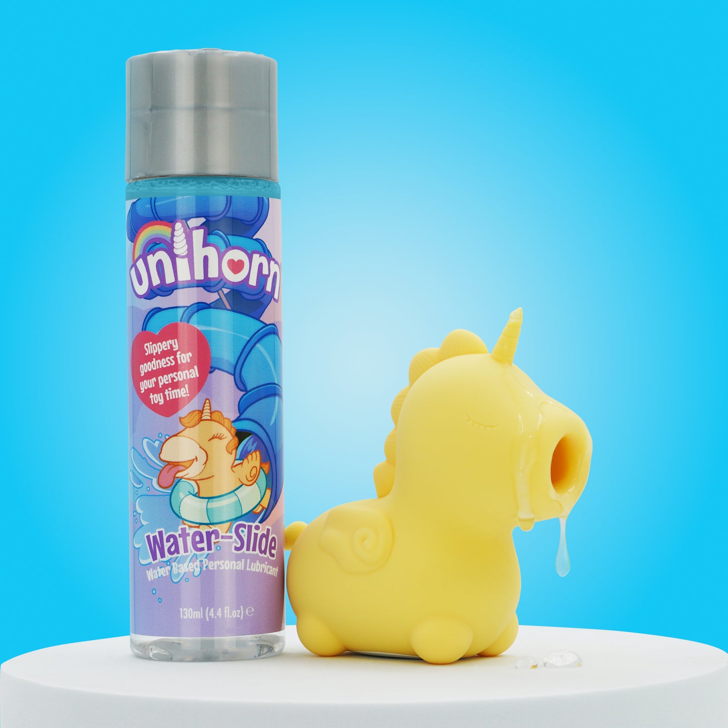 A bright blue background with a bottle of Unihorn lubricant stood next to Bean Blossom clitoral Unihorn vibrator with lube on the mouthpiece