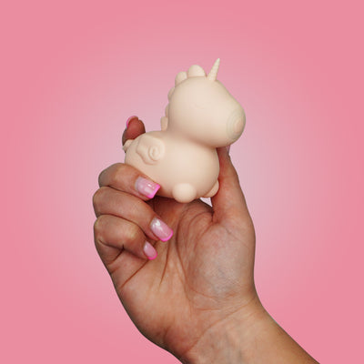 Hand holding a baby pink Heart Throb Unihorn vibrator on a pink background